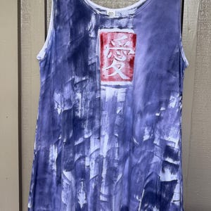 May include: A sleeveless tank top featuring a purple and white tie-dye pattern with a rectangular graphic on the chest. The graphic contains a red background with the white Japanese kanji character for love, which is written as 愛, centered on the fabric.