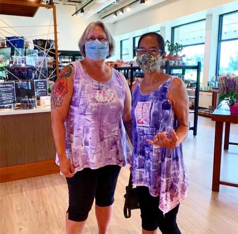 Puede incluir: Dos camisetas sin mangas con un patr&oacute;n abstracto de pinceladas en violeta y blanco. Cada prenda tiene un cuello redondo y un corte holgado y fluido. Las prendas se combinan con leggings negros tipo capri para un conjunto coordinado.