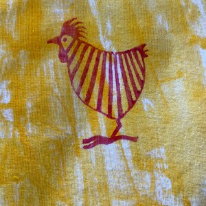 Op de afbeelding: Een gele stof met een rood gestileerd kippenontwerp erop gedrukt.