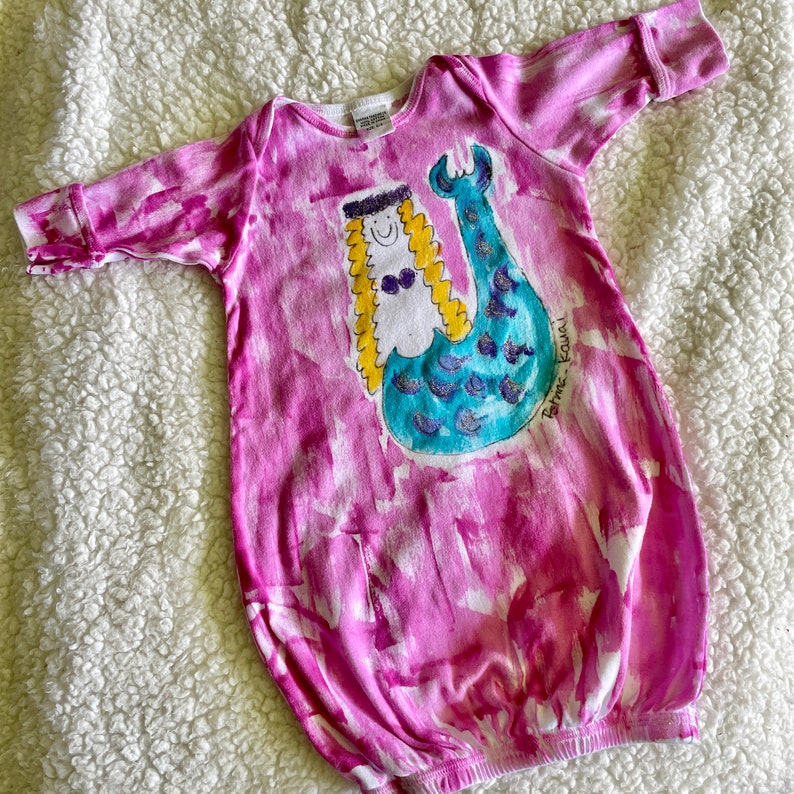 A pink and white hand painted baby gown with a mermaid illustration and signed by the artist and Kaua'i