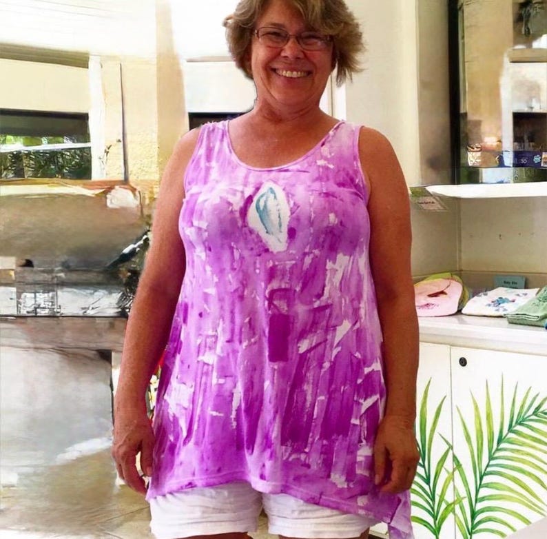 Puede incluir: Una camiseta sin mangas con un vibrante patr&oacute;n abstracto de pinceladas moradas y blancas con un acento central en forma de l&aacute;grima en blanco y azul claro, combinada con pantalones cortos blancos lisos.