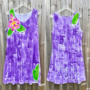 Peut inclure: Une robe sans manches avec un motif abstrait de coups de pinceau violets peints &agrave; la main. Le devant pr&eacute;sente une grande fleur rose et jaune avec des feuilles vertes, tandis que le dos montre une seule feuille verte pr&egrave;s de l'&eacute;paule.