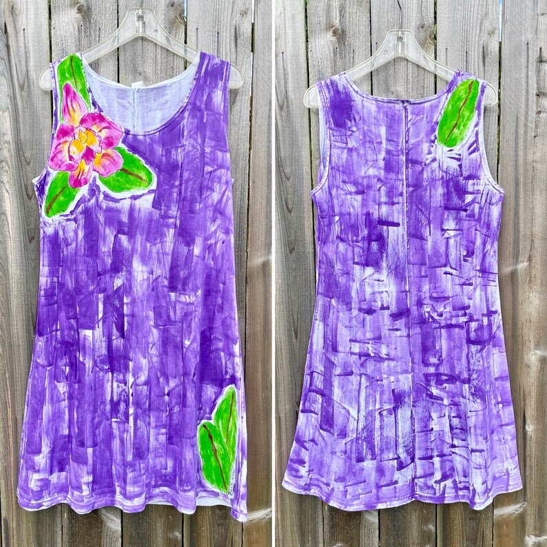 Peut inclure: Une robe sans manches avec un motif abstrait de coups de pinceau violets peints &agrave; la main. Le devant pr&eacute;sente une grande fleur rose et jaune avec des feuilles vertes, tandis que le dos montre une seule feuille verte pr&egrave;s de l'&eacute;paule.
