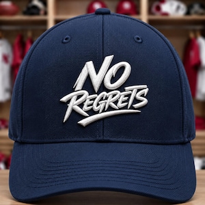 May include: A navy blue baseball cap featuring the white embroidered text NO REGRETS centered on the front panel. The cap has a structured crown, a curved brim, and stitched eyelets on the top panels, providing a clean and classic appearance.