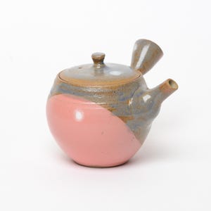 Peut inclure: Une théière en céramique de type kyusu avec un corps arrondi, une partie inférieure rose mat lisse et une partie supérieure texturée aux tons gris et bruns mouchetés. Elle comprend une poignée latérale, un bec court et un couvercle assorti.