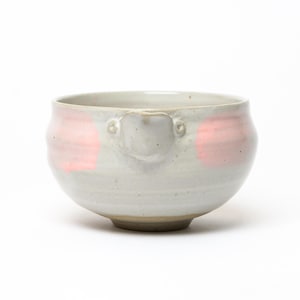 Peut inclure: Un bol en céramique avec une finition gris clair mouchetée et un petit bec verseur. L'extérieur présente deux taches circulaires rose pâle distinctes sur les côtés opposés, et la base est d'une couleur beige naturelle non émaillée.