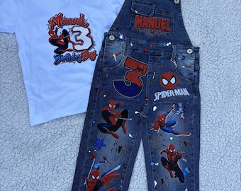 May include: A white short-sleeved t-shirt with a graphic featuring the name Manuel, the number 3, and Spider-Man, paired with dark blue denim overalls featuring Spider-Man graphics, the name Manuel, the number 3, and paint splatter details.