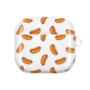 May include: A white protective case for wireless earbuds featuring a repeating pattern of cartoon hot dogs with yellow mustard. The case has a square shape with rounded corners and a small circular attachment loop on the right side for a lanyard.