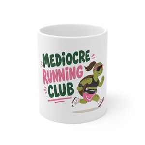 May include: A white ceramic mug featuring a graphic of a green turtle running. The turtle wears a black sports top, pink shorts, a ponytail, sunglasses, and a watch. The text reads MEDIOCRE RUNNING CLUB in dark green and pink lettering.