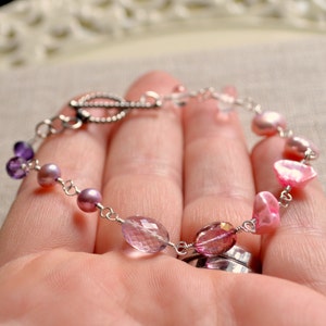 May include: A delicate bracelet with a silver chain and a variety of pink and purple gemstones, including amethyst, pearls, and pink quartz.