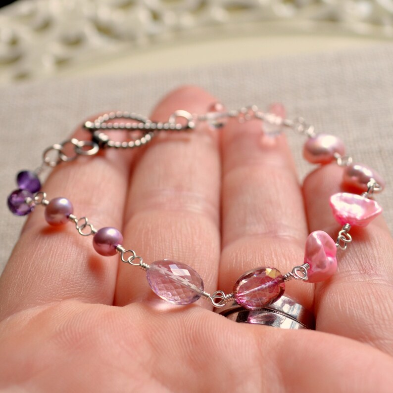 May include: A delicate bracelet with a silver chain and a variety of pink and purple gemstones, including amethyst, pearls, and pink quartz.