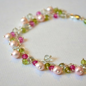 May include: A delicate silver chain bracelet with pink and green gemstone beads. The bracelet features a cascading design with multiple strands of beads.