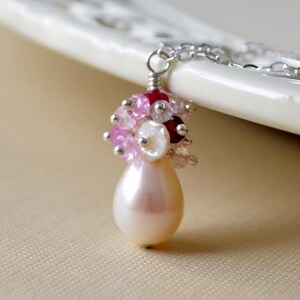 Puede incluir: Un delicado collar de cadena de plata con un colgante de lágrima nacarada. El colgante está adornado con un racimo de piedras preciosas rosas, blancas y rojas.