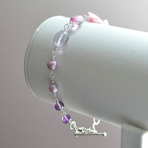 May include: A delicate bracelet featuring a mix of amethyst and freshwater pearls. The bracelet is made with silver wire and has a lobster clasp closure.