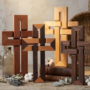 May include: Four wooden crosses with interlocking geometric designs, featuring varying shades of light, medium, and dark brown wood. The crosses are arranged in a group, with some placed on top of two stacked books titled Meditations.