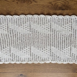 May include: A rectangular off-white crochet table runner featuring an intricate openwork pattern with diagonal lines and a scalloped edge border. The textile is crafted with fine thread and displays a repeating geometric design throughout the piece.