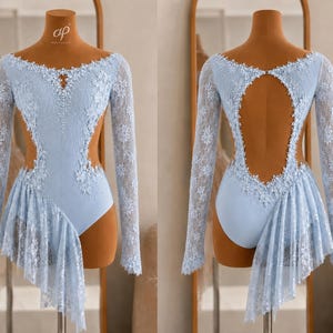 Könnte beinhalten: Ein hellblauer Langarm-Trikot mit weißer Spitzenauflage, Schlüsselloch-Ausschnitt und seitlich drapiertem Rock. Das Kleidungsstück ist mit verstreuten Kristallen entlang des Oberteils und der Spitzenkanten verziert und zeigt Vorder- und Rückansicht.