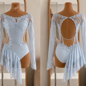 May include: A light blue long-sleeve leotard featuring intricate lace overlays, crystal embellishments along the neckline and bodice, side cutouts, and an asymmetrical lace skirt. The back displays a large circular cutout with a thin strap.