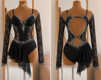 May include: A black leotard featuring long lace sleeves, a sweetheart neckline, and sheer mesh side panels. The garment is embellished with silver crystals and includes an asymmetrical lace skirt overlay. The back displays a large cutout design.