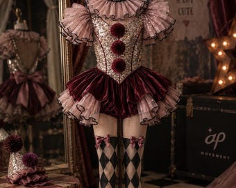 Könnte beinhalten: Ein Clown-Kostüm mit einem Pailletten-Oberteil, drei dunkelroten Bommeln, einem Rüschenkragen und einem mehrlagigen Samtrock. Das Outfit umfasst oberschenkelhohe Strümpfe mit schwarz-weißem Rautenmuster und kleinen Schleifen.