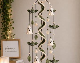 May include: A hanging mobile featuring crocheted white ghosts, olive green bats, and cream-colored stars suspended from a wooden ring. A central spiral element in olive green and cream connects the figures, accented with small wooden beads.