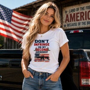 Può includere: Una t-shirt bianca a maniche corte con il testo "DON'T INFRINGE ON MY SECOND AMENDMENT" in blu e rosso, una grafica di un fucile su una bandiera americana invecchiata e la scritta "UNAPOLOGETIC AMERICAN" stampata sul fondo.