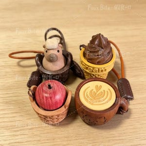May include: Four miniature charms featuring a capybara in a dark brown basket, a chocolate soft serve ice cream in a yellow cone with the text "Cream", a red apple in a light brown basket, and a coffee cup with latte art and a brown handle.
