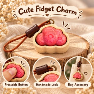 Op de afbeelding: Een wolkvormige fidget-bedel met een roze, houtnerf centrum in een lichtgekleurd houten frame. Het bevat een bruin leren koord met een donkerbruine schuifkraal. Tekst: Cute Fidget Charm, Pressable Button, Handmade Look, Bag Accessory.