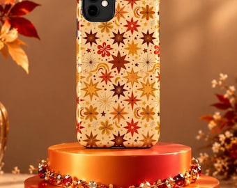 May include: A smartphone case featuring a repeating pattern of stars, suns, and crescent moons in shades of orange, yellow, brown, and cream. The case has a black camera cutout and is displayed upright on a tiered orange stand with crystal accents.