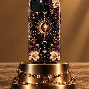May include: A black smartphone case featuring a central gold sun and crescent moon emblem surrounded by intricate gold filigree, starbursts, and clusters of white and deep purple flowers against a dark background with a dual-camera cutout.