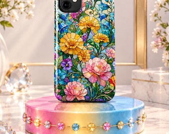 May include: A smartphone case featuring a vibrant, multi-colored floral pattern reminiscent of stained glass. The design includes yellow, pink, and blue flowers with green foliage, set against a dark, grid-like background. The case has a black camera cutout.