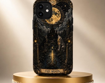 May include: A black smartphone case featuring a detailed tarot card illustration titled THE MOON. The design depicts a full moon, a castle, two wolves, and a winding path in dark tones with gold accents, including the Roman numeral XVIII.