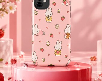 May include: A light pink smartphone case featuring a repeating pattern of white cartoon rabbits, red strawberries, small yellow flowers, and tiny hearts. The case has a black camera cutout at the top left corner and a smooth, glossy finish.