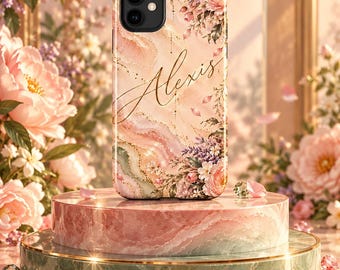 May include: A smartphone case featuring a pink and cream marbled pattern with gold accents and floral illustrations. The name Alexis is printed in a gold cursive script across the center of the case. The case has a dual-lens camera cutout.