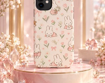 May include: A cream-colored smartphone case featuring a repeating pattern of white cartoon rabbits, pink tulips, small flowers, and light pink bows. The design includes illustrations of rabbits holding bouquets, reading books, and sitting, all rendered in a soft pastel color palette.