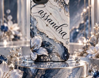 May include: A smartphone case featuring a blue and white marble pattern with gold accents, white floral illustrations, and the name Cassandra written in black script. The design includes small embedded crystals and a dual-lens camera cutout.