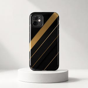 May include: A black smartphone case featuring a diagonal design with a wide gold stripe and thinner gold lines. The surface includes a textured section with fine parallel grooves, and the camera cutout is located in the upper left corner.