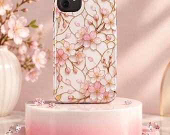 May include: A smartphone case featuring a white background with a delicate pattern of pink cherry blossoms and gold-colored branches. The design includes small, raised floral details and a dual-lens camera cutout at the top left corner of the case.