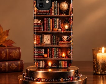 May include: A smartphone case featuring a printed design of a wooden bookshelf filled with colorful books, a globe, small pumpkins, a lantern with a lit candle, and a mug. The text on the books includes Autumn Days, Good Books, and Read More Worry Less.