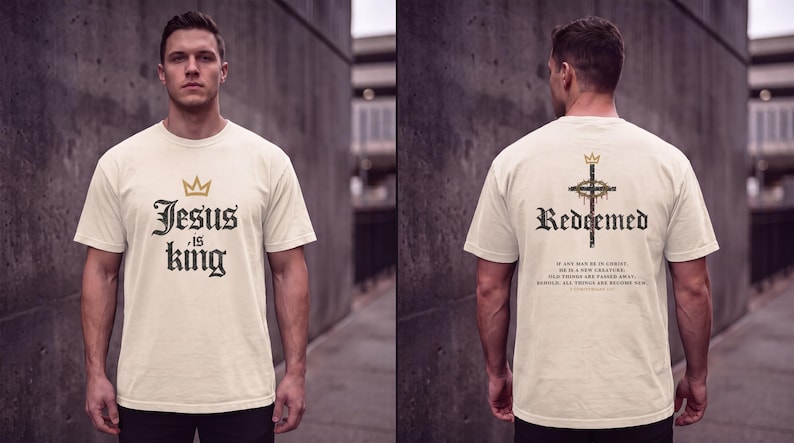 Op de afbeelding: Een cr&egrave;mekleurig T-shirt met korte mouwen. De voorkant heeft een gouden kroonicoon boven de zwarte tekst "Jesus is king". De achterkant toont een kruis met een kroon, het woord "Redeemed" en het vers 2 Corinthians 5:17 in zwarte tekst.