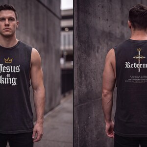 May include: A charcoal grey sleeveless muscle tank top featuring a gold crown icon and the white text Jesus is King on the front. The back displays a cross graphic with a crown, the word Redeemed, and additional small white text.