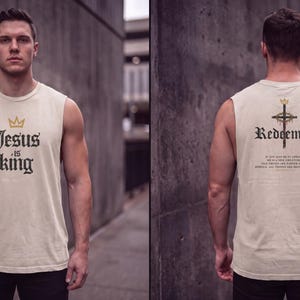 May include: A beige sleeveless shirt featuring a gold crown icon and the black text "Jesus is King" on the front. The back displays a gold crown, a cross graphic, the word "Redeemed," and additional small text printed in black.