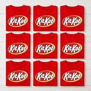 May include: Nine bright red t-shirts arranged in a three-by-three grid. Each shirt features the KitKat logo printed in white text with a bold yellow oval outline centered on the chest. The shirts are folded neatly with a crew neckline visible.