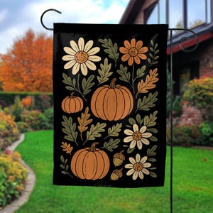 May include: A rectangular garden flag with a black background featuring a repeating pattern of orange pumpkins, cream and orange daisy-like flowers, green oak leaves, and small brown acorns arranged in a decorative seasonal display.