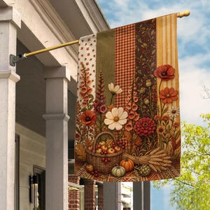May include: A vertical garden flag featuring a harvest theme with vertical stripes of plaid, floral patterns, and solid colors. The design displays a woven basket filled with apples, surrounded by tall flowers, wheat stalks, and pumpkins.