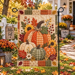 May include: A rectangular garden flag featuring a quilted design of three pumpkins in orange, cream, and green. The pumpkins are surrounded by sunflowers, autumn leaves, and berries on a cream background with a patchwork border of plaid and floral patterns.