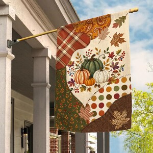 May include: A decorative garden flag featuring a patchwork design of autumn-themed patterns including plaid, paisley, polka dots, and herringbone. The central graphic displays a collection of pumpkins, colorful fall leaves, and berries.