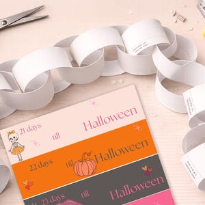 May include: A paper chain made of white loops arranged in a semi-circle above a printed sheet. The sheet features horizontal sections with text and graphics, including a skeleton, a pumpkin, and the repeated phrase "days till Halloween".