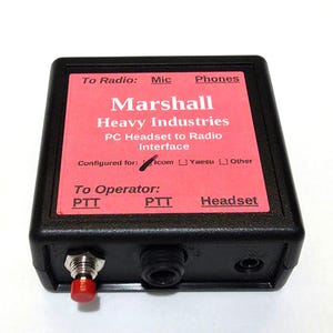 May include: A black rectangular radio interface box with a red label featuring the text Marshall Heavy Industries PC Headset to Radio Interface. The front panel includes a red push-button switch, a central port, and a small circular input jack.