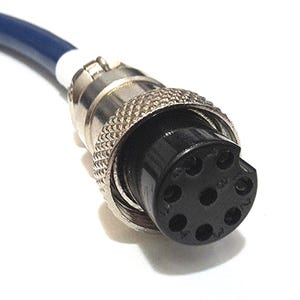 Puede incluir: Un conector eléctrico circular con un anillo de bloqueo metálico moleteado y un inserto de plástico negro que presenta seis orificios para pines dispuestos en círculo. El conector está unido a un cable azul oscuro con una funda blanca.